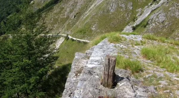 Sentiero lastricato su un versante montuoso, con un tronco di legno che spunta dalla pietra. Un percorso che ricorda le antiche vie, come quelle delle **via Vandelli tappe**.