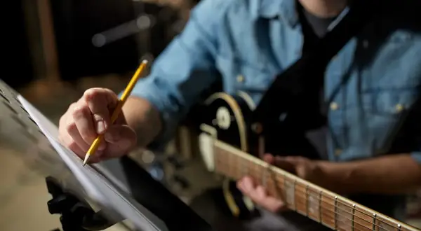 Muzyk w dżinsowej koszuli poprawia nuty, by uchwycić idealny groove. Gitara czeka na swój moment.