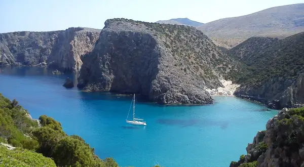 Baia con acque cristalline e una barca a vela. Le scogliere rocciose e la vegetazione mediterranea creano uno scenario suggestivo, perfetto per capire come si misura la profondità del mare.