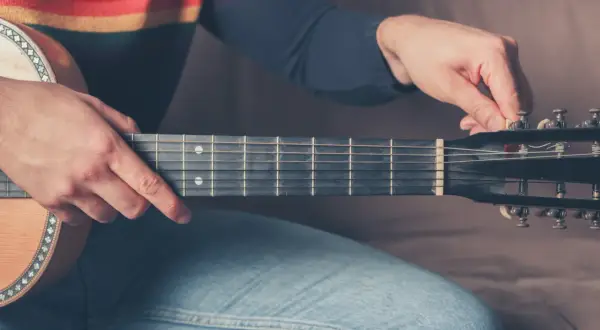 Dłoń stroi gitarę 12 strunową, naciągając struny.