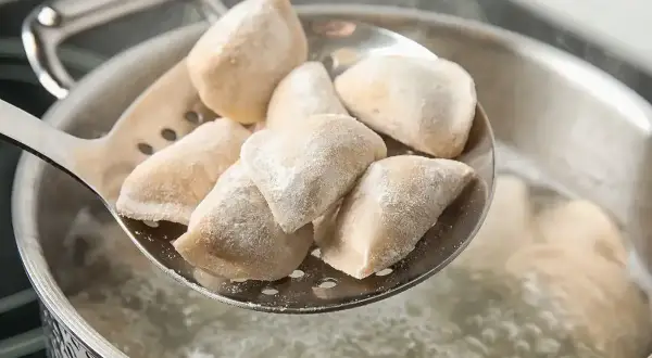 Jak gotować mrożone pierogi? Na łyżce cedzakowej świeżo wyjęte z wrzątku, parujące pierożki.
