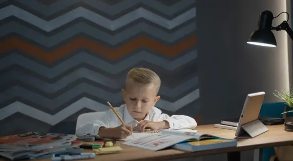 Chłopiec pochyla się nad zeszytem, pisząc ołówkiem. Idealna wysokość biurka dla dziecka zapewnia komfort nauki.