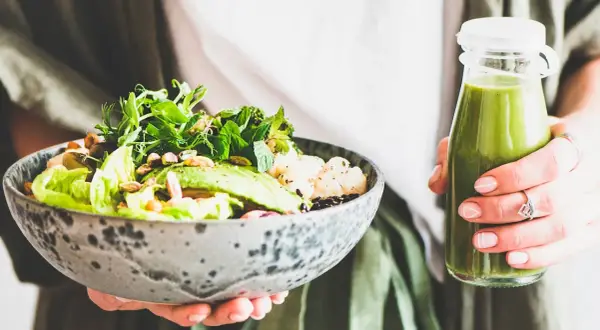 En person håller en skål med en hälsosam sallad och en grön smoothie. Perfekt bra mat gravid för näring och energi.