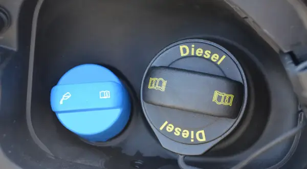 Dwa korki wlewu paliwa: jeden niebieski z symbolem płynu i książki, drugi czarny z napisem "Diesel" i symbolami. Dowiedz się, adblue co to jest i do czego służy.
