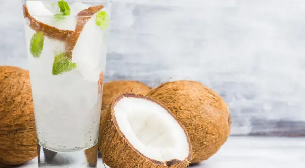 Orzeźwiający drink z wodą kokosową, lodem i miętą, obok świeżych kokosów. Idealny na upalne dni.