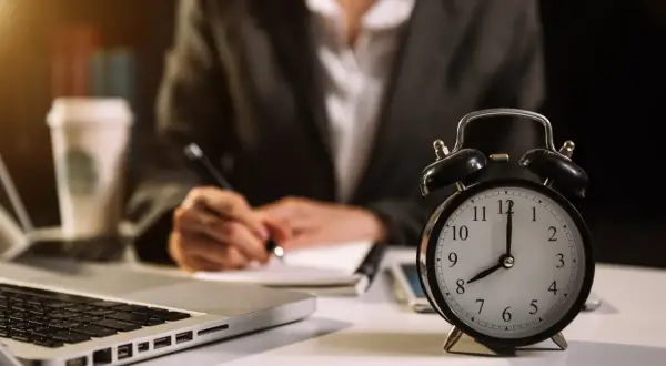 Budzik pokazuje 8:00, a osoba pisze w notatniku. Ile godzin pracy jeszcze przed nią?