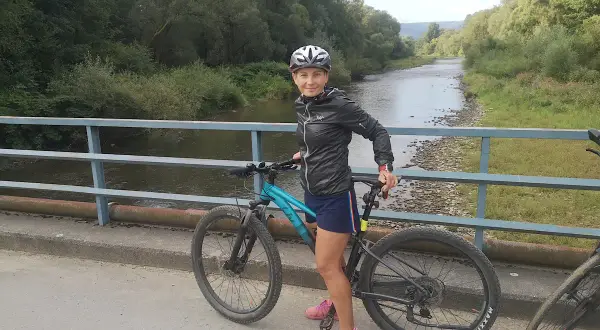 Kobieta na rowerze na moście, gotowa do odkrywania malowniczych velo tras rowerowych wzdłuż rzeki.