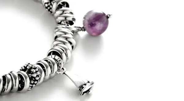 Pulsera de plata con charms, destacando una cuenta de amatista púrpura y un charm en forma de campana.