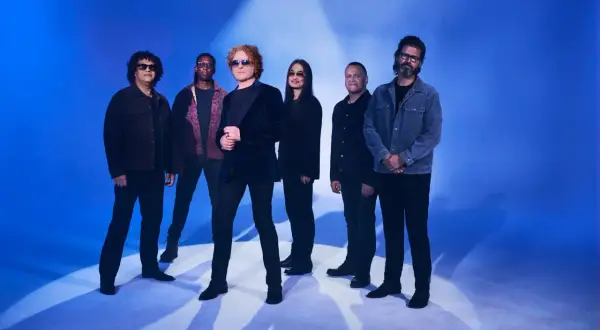 Zespół Simply Red gotowy na koncert. Muzycy pozują na tle niebieskiego światła, tworząc atmosferę nadchodzącego wydarzenia.