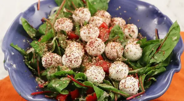 En blå skål med en sallad av gröna blad, körsbärstomater och små, kryddade labneh bollar.