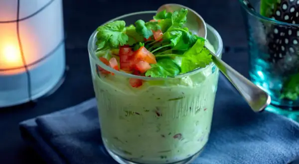 Krämig guacamole med crème fraîche, toppad med färsk koriander och tärnad tomat. Serveras i ett glas med en sked.