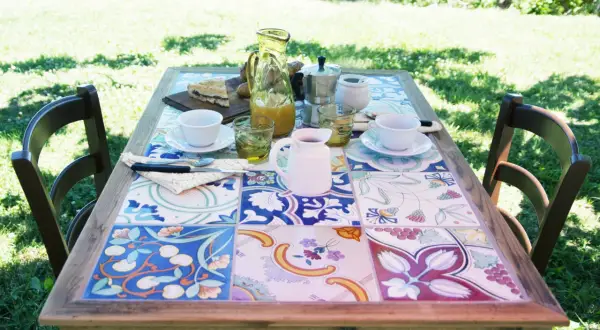 Tavolo con piastrelle fai da te, perfetto per un brunch all'aperto. Colori vivaci e motivi floreali creano un'atmosfera allegra.