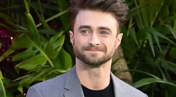 Daniel Radcliffe, który grał Harry'ego Pottera, w szarym garniturze na tle zieleni.