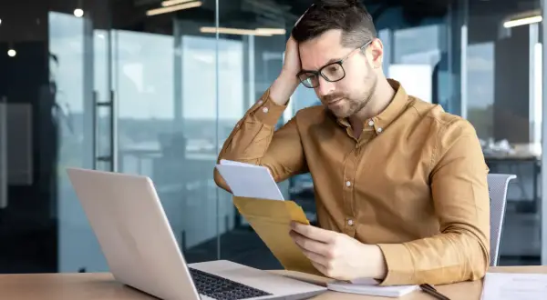 Uomo preoccupato legge una lettera di richiamo per ferie non concordate, con un laptop aperto davanti a sé.