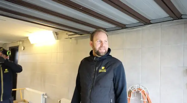 Man i väst med texten "Garageportexperten" ler. Ovanför syns en **täta garageport** i taket.