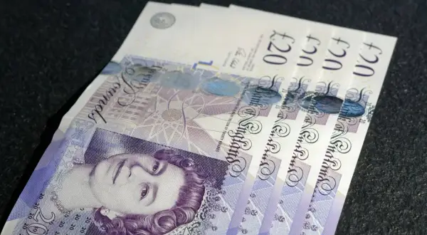 £ co to za waluta? Kilka banknotów po 20 funtów brytyjskich leży na ciemnym tle.