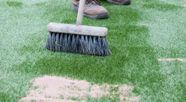 Cepillo extendiendo arena de sílice para césped artificial. Mantenimiento del césped sintético.