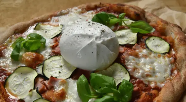 Pyszna pizza z burrata, cukinią i bazylią, posypana świeżo mielonym pieprzem.