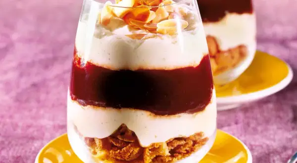 Schichtdessert im Glas mit zerbröselten Amarettini, roter Fruchtsauce und cremiger Masse, garniert mit Mandelblättchen.