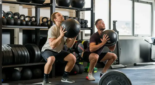 Deux hommes font des squats avec des medecine balls. Un bon sport pour maigrir et se muscler.