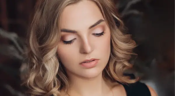 Delikatne, świąteczne makijaże podkreślają urodę blondynki z kręconymi włosami.