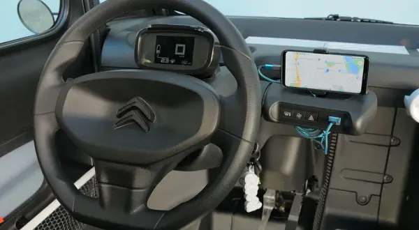 Interno Citroen Ami: volante, cruscotto digitale con indicatore di velocità e autonomia, smartphone con navigatore. La velocità massima è un dettaglio da scoprire!