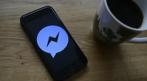 Telefon z ikoną Messengera na ekranie, obok kubek kawy. Dowiedz się, jak ustawić dźwięk powiadomienia Messenger.