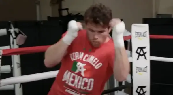 Boxer in a red "Team Canelo Mexico" shirt practices shadow boxing in a ring, his fists wrapped and ready.