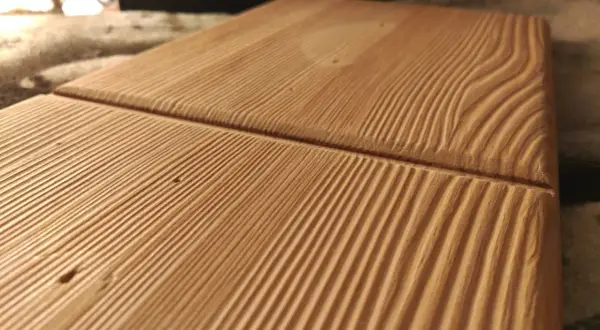 Superficie de madera con surcos paralelos que resaltan las vetas naturales. La luz crea sombras que dan profundidad a la textura.