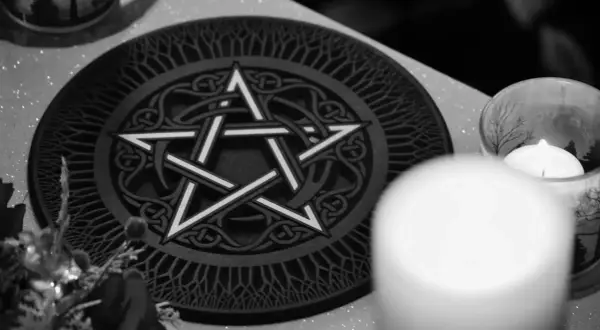 Oto jak wygląda pentagram: pięcioramienna gwiazda wpisana w okrąg, ozdobiona celtyckimi wzorami. Obok świeca w szklanym naczyniu.