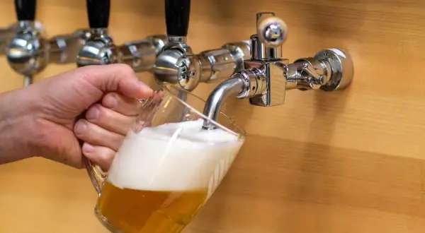 Mano che versa una birra dorata con schiuma abbondante da un rubinetto cromato. La birra alder è pronta da gustare.