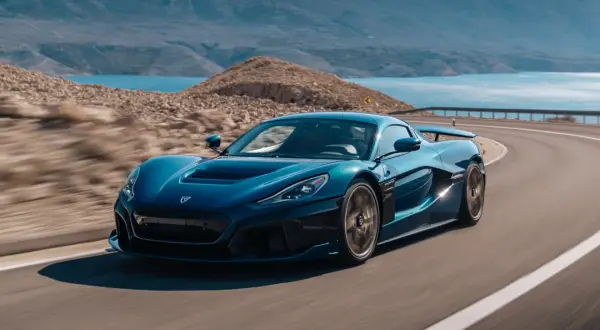 Niebieski Rimac Nevera sunie po krętej drodze nad turkusowym morzem, otoczony skalistym krajobrazem.