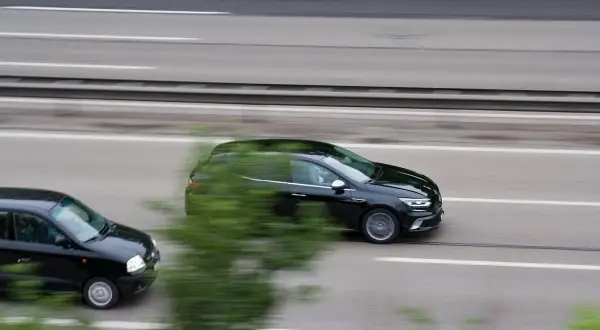 Czarny samochód wyprzedza inny pojazd na autostradzie.