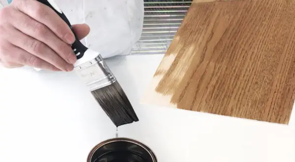 Pennello intinto in latta di impregnante, pronto per applicarlo su un campione di legno.