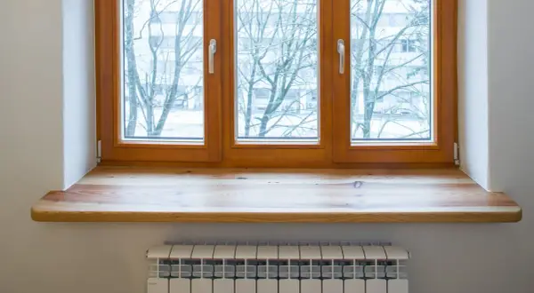 Neue Fensterbank aus Holz, auf die alte geklebt, mit Blick auf Bäume im Winter. Heizkörper darunter.