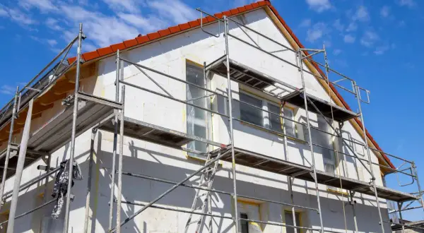 Gerüst um Haus für Fassaden Sanierung. Weiße Wände, rote Ziegel und blauer Himmel.