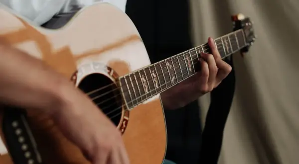 Dłoń grająca na gitarze akustycznej. Czy gra na gitarze jest trudna? Zależy od determinacji i praktyki!