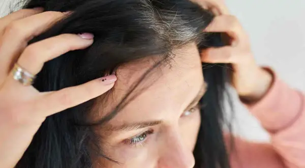 Mani che toccano i primi capelli bianchi tra i capelli scuri, un segno del tempo che passa.