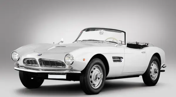 Biały kabriolet BMW 507 z lat 50. prezentuje się elegancko na szarym tle.