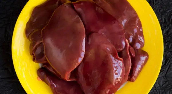Surowa wątróbka na żółtym talerzu. Czy wątróbka jest tłusta? Wygląda na soczystą i gotową do smażenia.