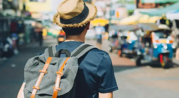 Mężczyzna w kapeluszu i z plecakiem na tle tętniącego życiem azjatyckiego miasta. Poznaj jego travel hacks!