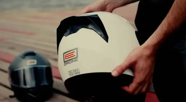 Ręce trzymają biały kask motocyklowy. Obok leży czarny kask. Dylemat: kask szczękowy czy integralny?