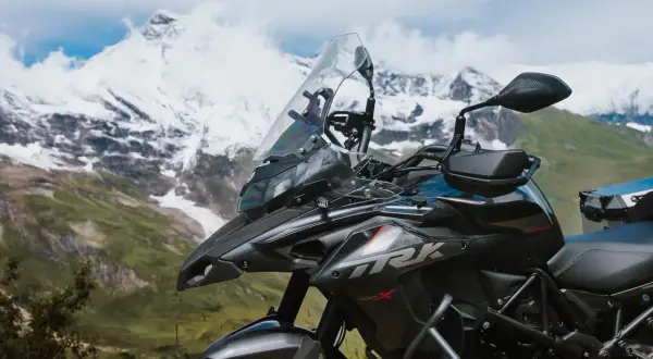 Ciemny motocykl turystyczny na tle ośnieżonych gór i zielonej doliny.