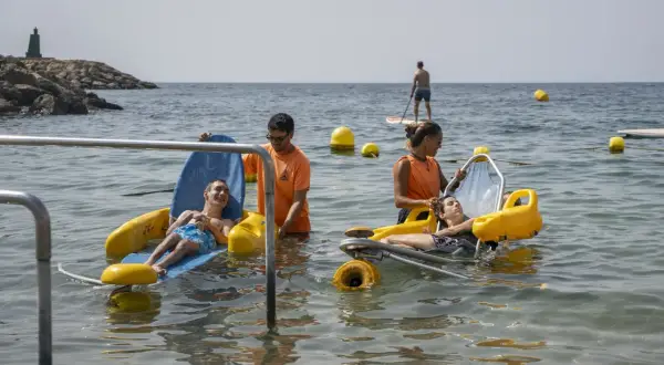 Socorristas ayudan a personas en sillas anfibias en la playa de Aguadulce. Un hombre hace paddle surf al fondo.
