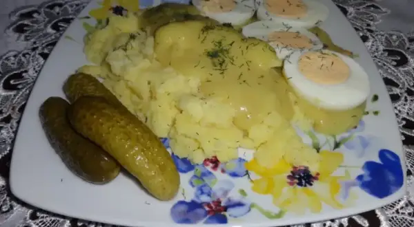 Talerz z ziemniakami puree, jajkami na twardo i ogórkami kiszonymi, polany sosem musztardowym.