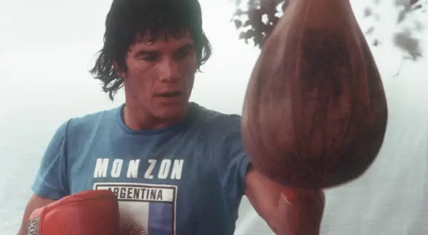 Carlos Monzón, the legendary boxer, trains with a speed bag, his blue shirt bearing his name and the Argentine flag.