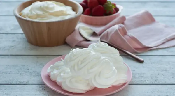 Creme double auf einem rosa Teller, daneben eine Schüssel mit Erdbeeren und ein Holzlöffel.