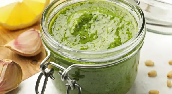 Domowe pesto w słoiku, obok czosnek i cytryna. Czy pesto ze słoika się podgrzewa? Zwykle nie, ale to zależy od przepisu.