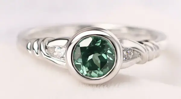 Anillo de plata con piedra verde ovalada y dos pequeños diamantes a cada lado, sujeto con un engaste bisel.