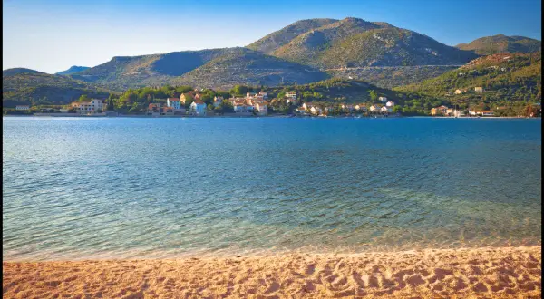 Słoneczna plaża i spokojne morze w Słano, Chorwacja. W oddali widać urokliwe **małe wyspy chorwackie** i zielone wzgórza.